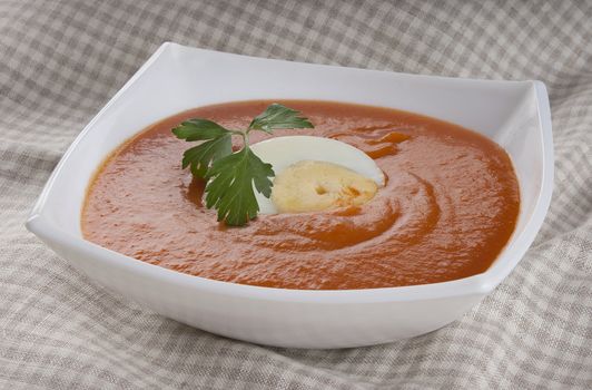 Tomato soup with parsley and boiled egg in white bowl