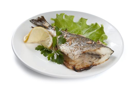 Baked sea bream with lettuce, lemon and parsley on the white plate