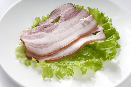 Some pieces of bacon with lettuce on the white plate