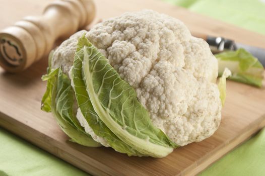 Head of cauliflower on the wooden board with peppermill and knife