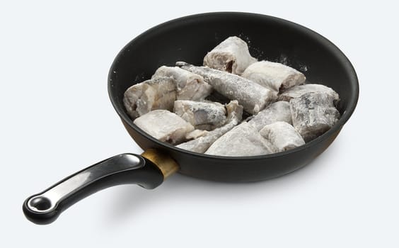 Raw flour coated pieces of pollack on the black frying pan