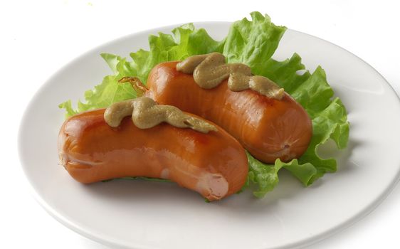 Two roasted small sausages with lettuce and mustard on the plate