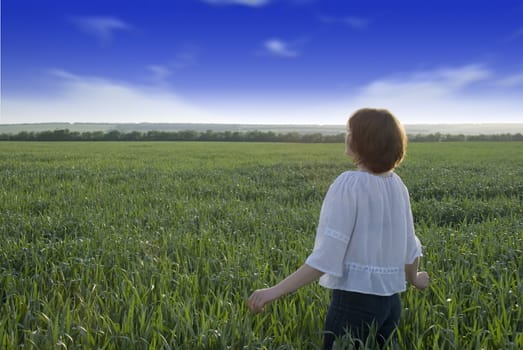The girl on a meadow. A field of wheat, the contrast sky and the girl looking in a distance