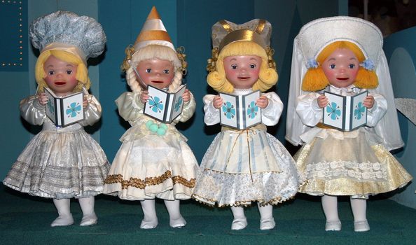 Four dolls singing in a row with matching outfits.