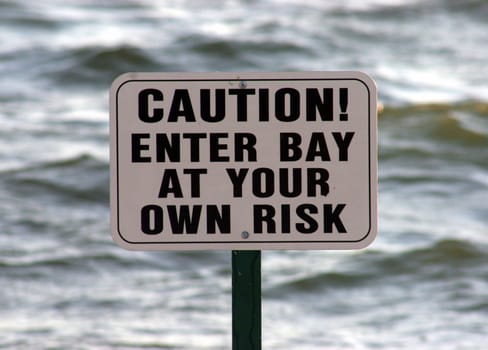 Caution sign with sea behind taken on a beach.