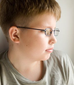 little serious boy in glasses near a window