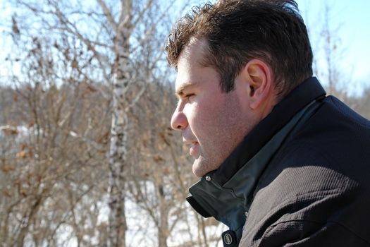 Winter. The young man in a profile against birches.