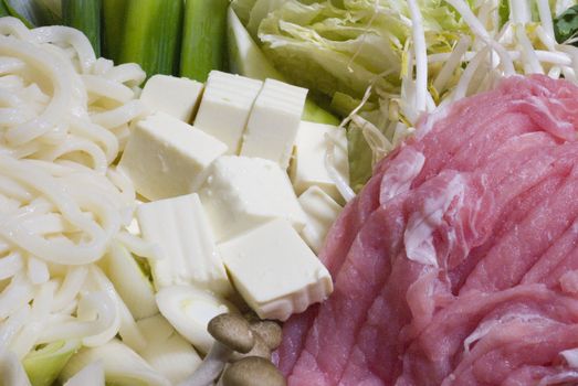 Noodles, tofu, pork and other ingredients spread out prepared for shabu shabu. white and red horizontal