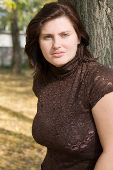 The young beautiful woman near a tree in autumn park.
