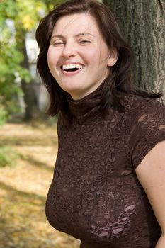 Smiling beautiful woman near a tree in autumn park.