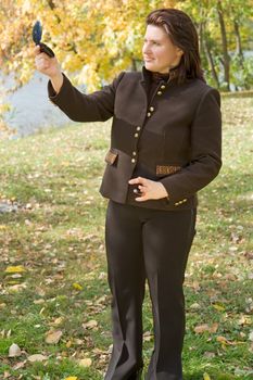 young beautiful woman looks in a pocket mirror against autumn park