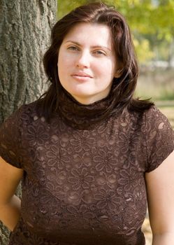 The young beautiful woman near a tree in autumn park.