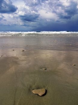 stone in the form of heart lies in the wet sand at low tide