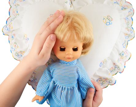 Children's hands holding a doll lying on the pillow