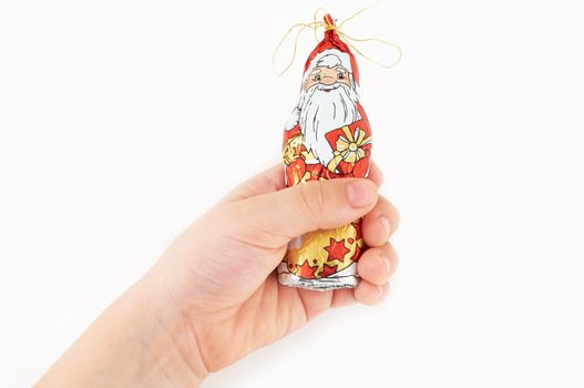 Children's hand holding a Christmas decoration in the form of a chocolate Santa Claus figures on an isolated white background