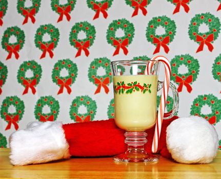 A glass of Christmas eggnog on a table with a wreath background and a Santa cap using selective focus and a shallow depth of field