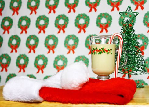 A glass of Christmas eggnog on a table with a wreath background and a Santa cap and Christmas tree using selective focus and a shallow depth of field