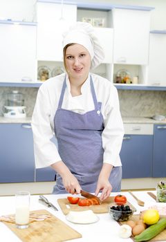 Attractive chief cook preparing food, cutting tomatoes