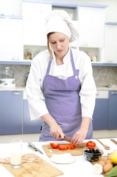 Attractive chief cook preparing food , cutting tomatoes
