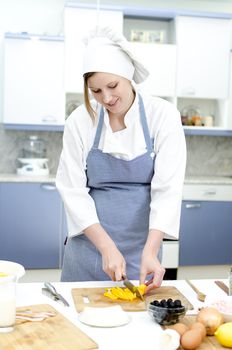 Attractive chief cook preparing food , cutting paprika