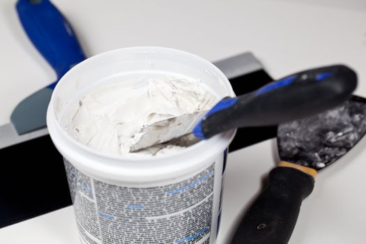 Knife in patching plaster in plastic tube with other tools on the floor