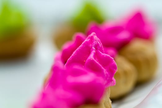 Close up view of the pink color icing topped cookies with green icing cookies in background
