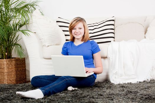young teenager girl with laptop smilig ssitting on couch 