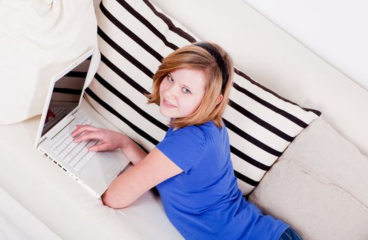 young teenager girl with laptop smilig ssitting on couch 