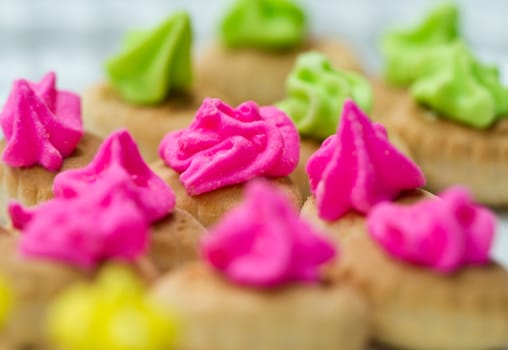 Close up view of the pink color icing topped cookies with green icing cookies in background and yellow in the foreground