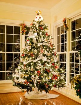 Christmas tree decorated with silver and white ribbons and ornaments in family home