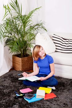 teenager girl sitting on the floor with lot of books and doing homework learning reading