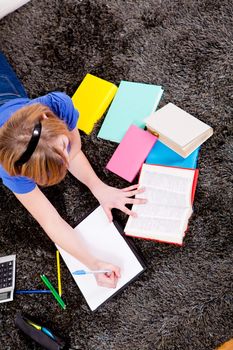 teenager girl sitting on the floor with lot of books and doing homework learning reading