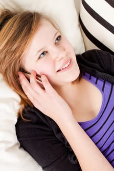 teenager girl smiling and lying on couch with mobile phone and talking