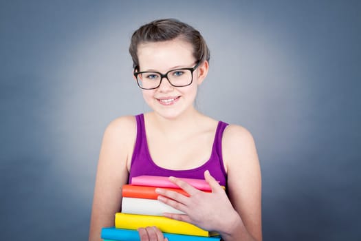 Silly smiling schoolgirl with glasses and lots of books having fun