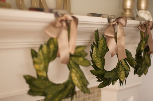 three green wreaths hanging with gold ribbon from a white mantle