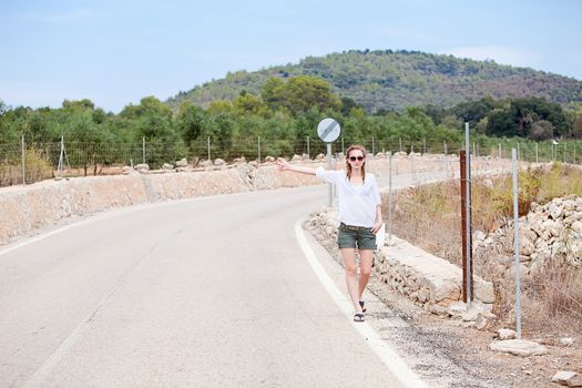 attractive blond woman in summer holiday walking a road stopping car tramping journey