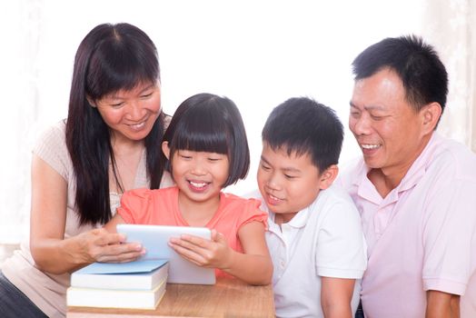 Asian family at home. Parents and children using digital tablet computer together.