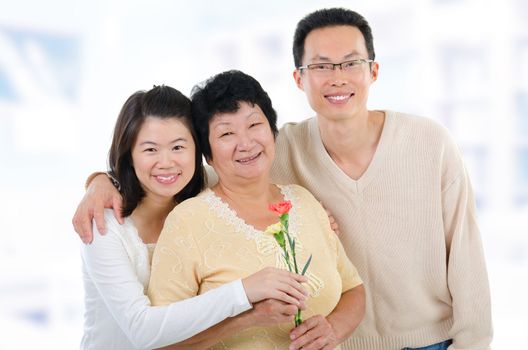 Asian family at home. Adult offsprings giving carnation flowers to senior mother.