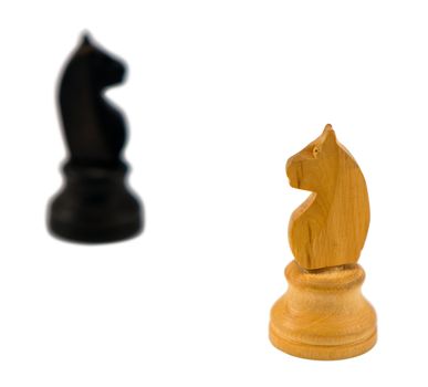 white wooden chess knight figure and blurred black one in distance on white background