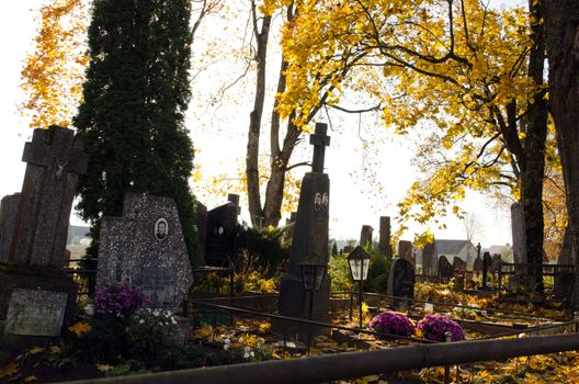 cemetery graveyard grave crosses stoneheads monument under autumn tree leaves.