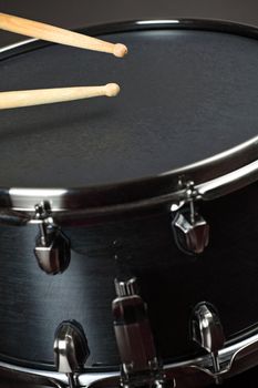 Drumsticks playing on a wood snare with black drum skin.