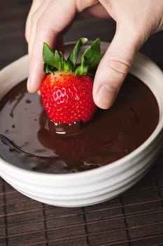 Hand dipping fresh strawberry in melted chocolate