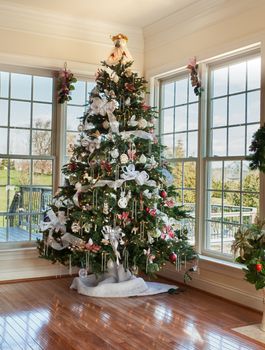 Christmas tree decorated with silver and white ribbons and ornaments in family home