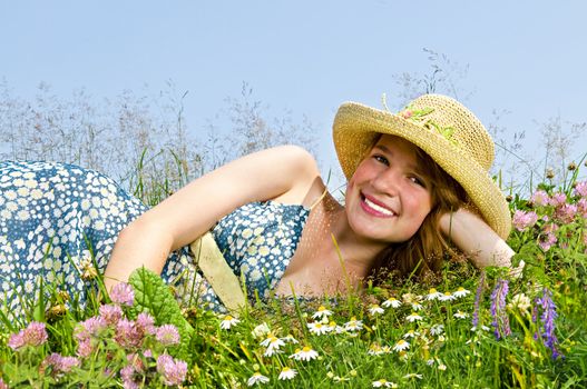 Young teenage girl laying on summer meadow amid wildflowers in straw hat