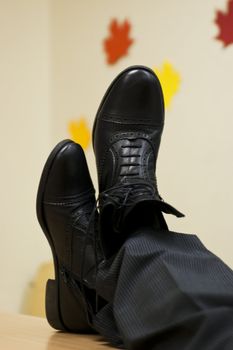 Maded of black leather shoes crossed on table