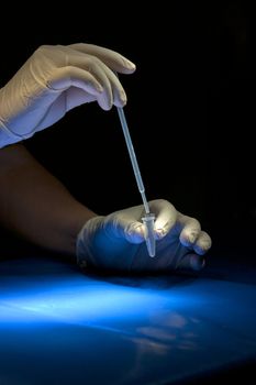 Hands in white gloves hold pipette and tube