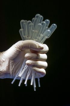 Hand in white gloves holding many empty pipettes