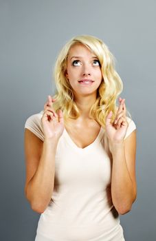 Blonde caucasian woman wishing with fingers crossed on gray background