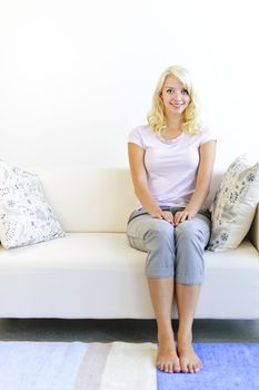 Pretty blonde woman sitting on sofa at home smiling
