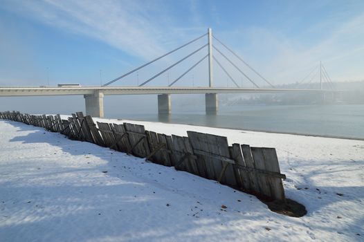 Winter morning by Danube river with bridge in fog